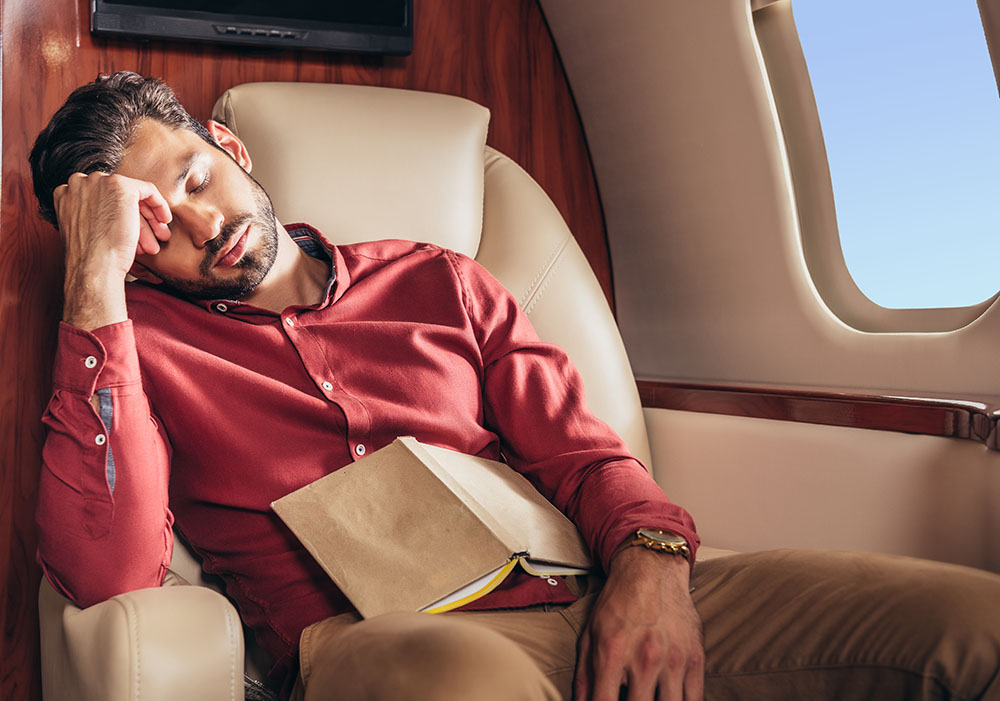 handsome man in shirt sleeping with book in private plane