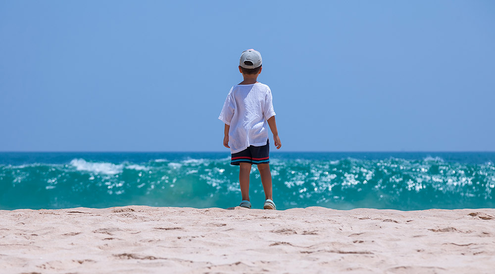 A boy on a tropical beach looking out at an endless horizon